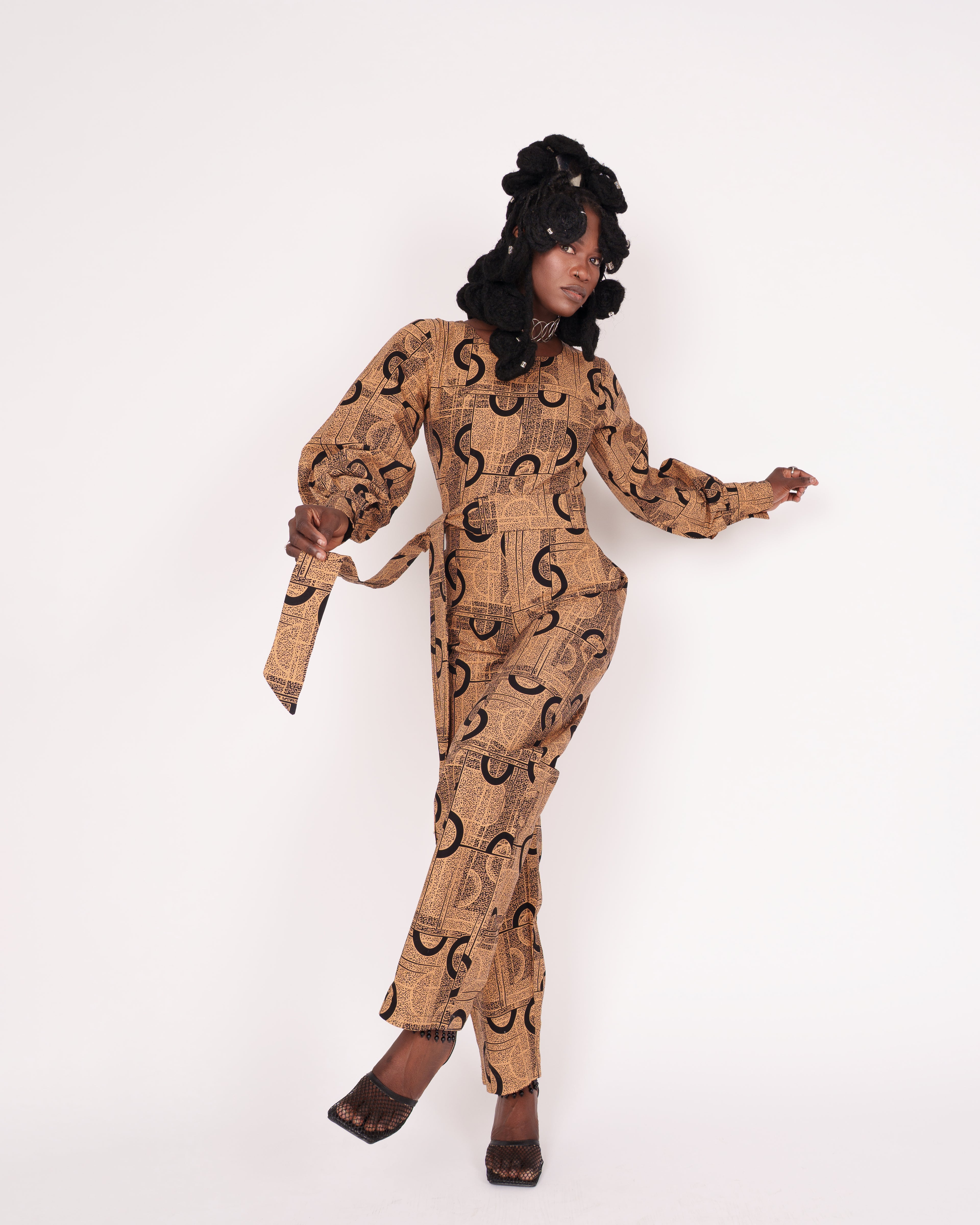 Jumpsuit featuring long balloon sleeves, a fitted waist with a detachable belt, and straight ankle-length pants adorned with an abstract pattern.