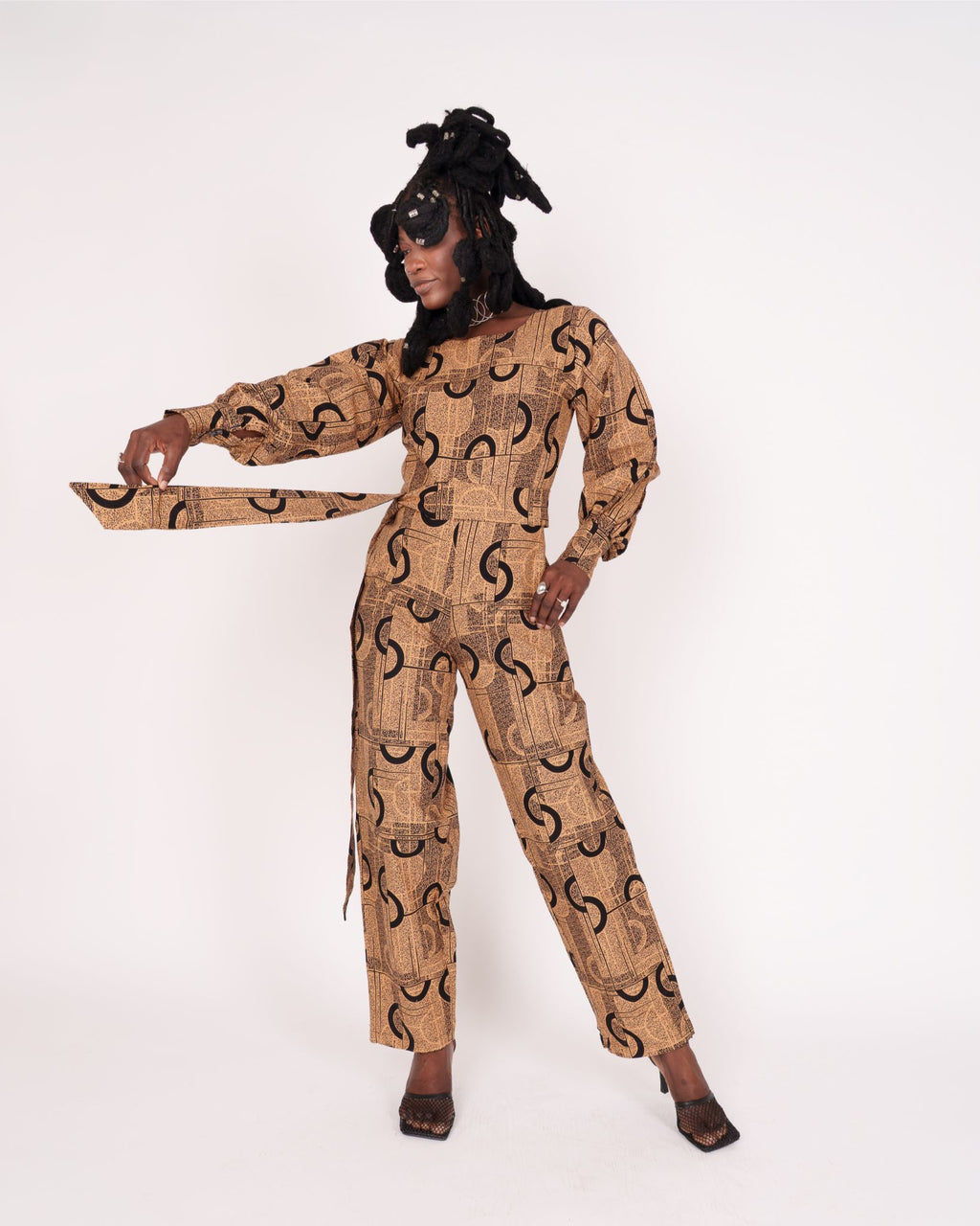 Jumpsuit featuring long balloon sleeves, a fitted waist with a detachable belt, and straight ankle-length pants adorned with an abstract pattern.