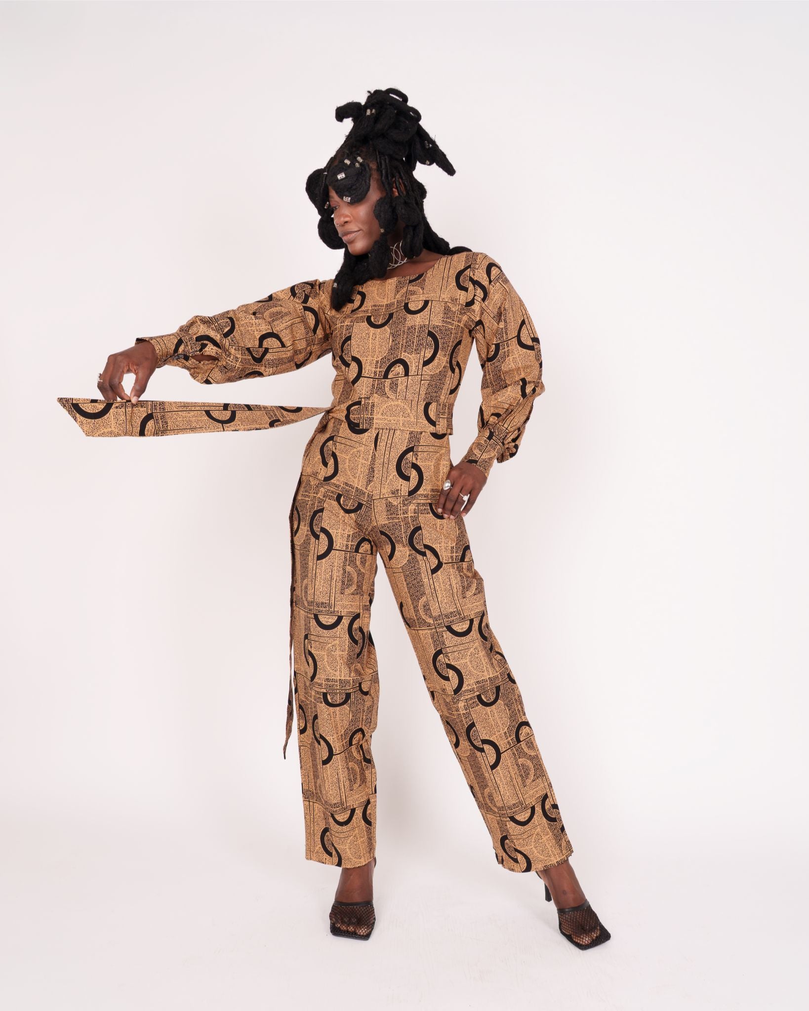 Jumpsuit featuring long balloon sleeves, a fitted waist with a detachable belt, and straight ankle-length pants adorned with an abstract pattern.