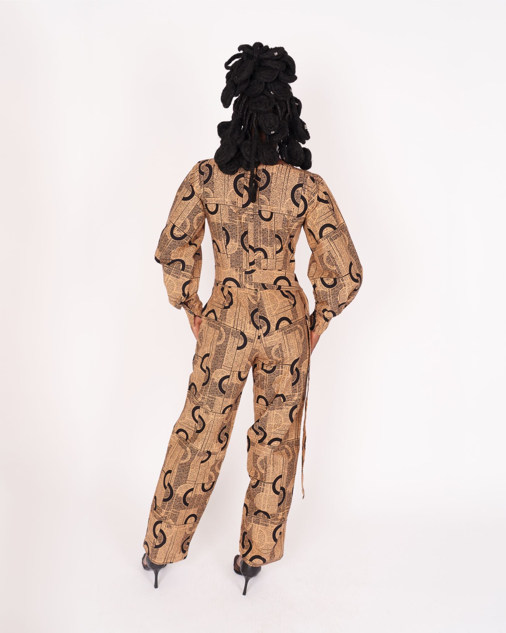 Jumpsuit featuring long balloon sleeves, a fitted waist with a detachable belt, and straight ankle-length pants adorned with an abstract pattern.