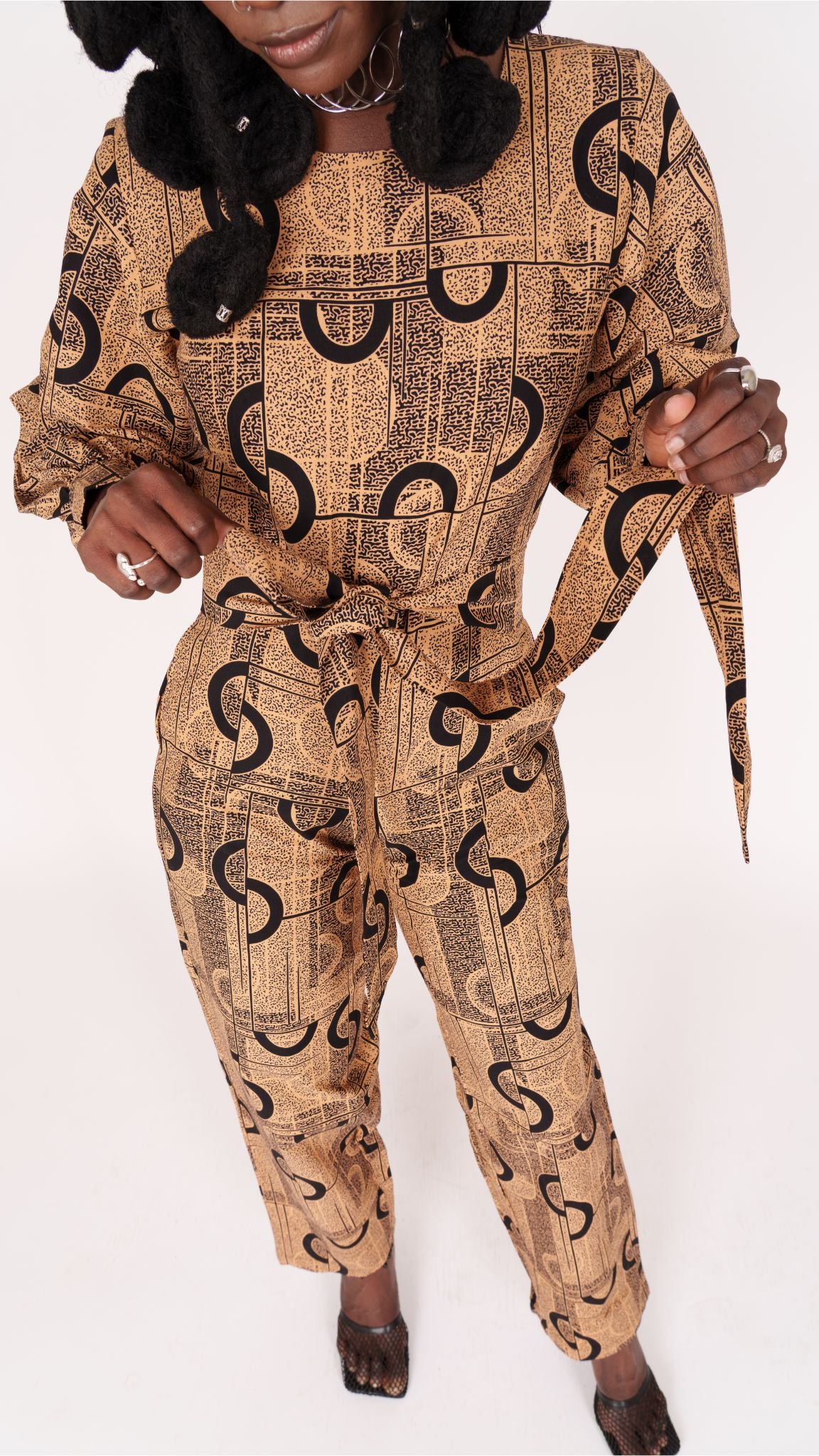 Jumpsuit featuring long balloon sleeves, a fitted waist with a detachable belt, and straight ankle-length pants adorned with an abstract pattern.